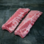 Rohe Baby Back Ribs vom regionalen Duroc-Schwein, präsentiert auf Schieferplatte.