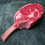 Imposantes US Tomahawk Steak mit langem Knochen für Gezer Gastro-Kunden, präsentiert auf Schieferplatte.