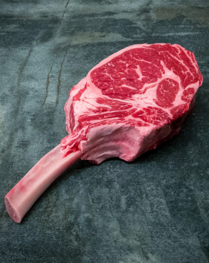 Imposantes US Tomahawk Steak mit langem Knochen für Gezer Gastro-Kunden, präsentiert auf Schieferplatte.