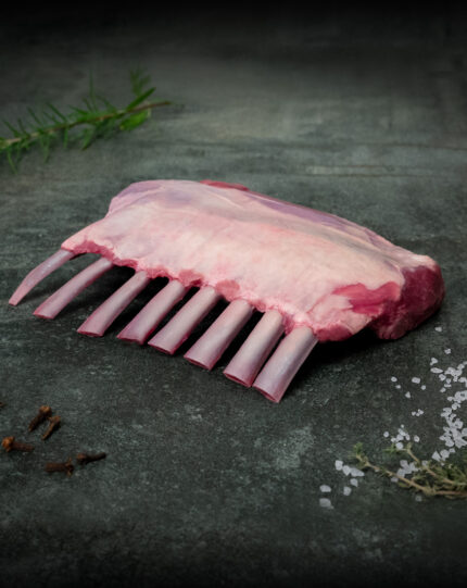 Rohes Lammkarree auf einer dunklen Schieferplatte mit Kräutern angerichtet für die Gastronomie.