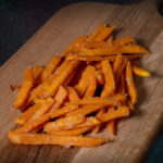 Süßkartoffel-Pommes, leuchtend orange auf einer Schieferplatte präsentiert für Gezer Kunden.