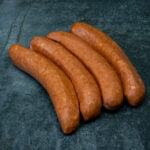 Original Käsekrainer aus Österreich, goldbraun auf einer Schieferplatte präsentiert für Gezer Kunden.